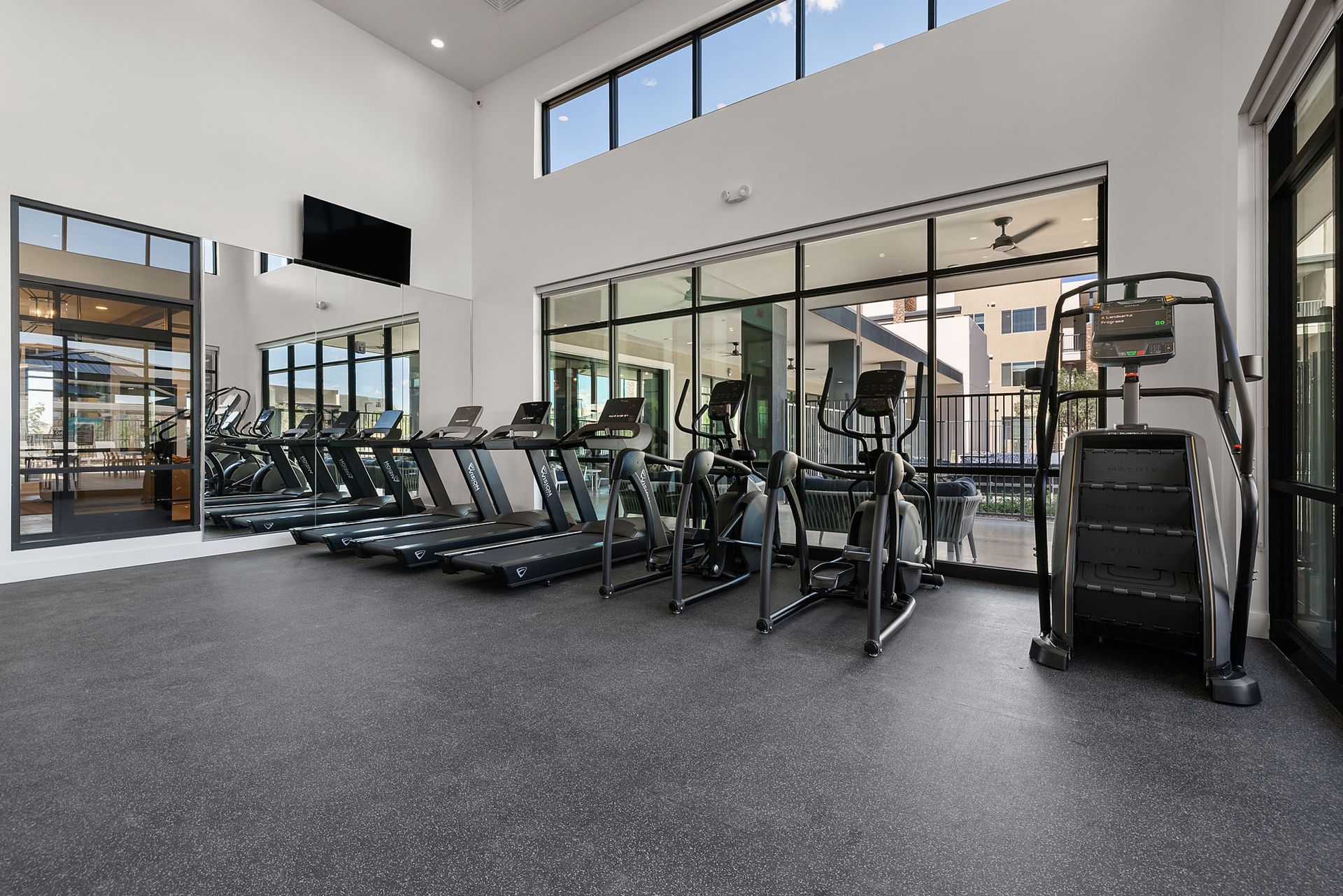 Gym with treadmills, ellipticals, and a stair climber near large windows, with a dark gray floor at Marq Bronco Butte.