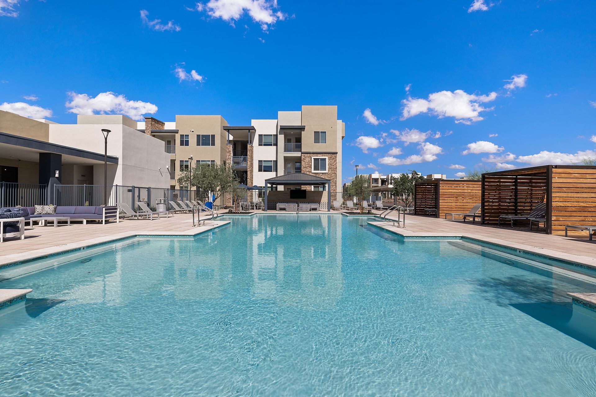 Swimming pool in front of apartment buildings on a sunny day with blue sky and white clouds at Marq Bronco Butte, offers brand-new apartments near TSMC in North Phoenix, AZ.