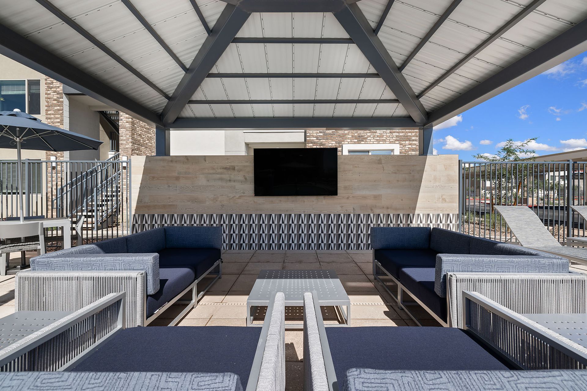 Outdoor lounge area with couches, TV, and overhead shelter at Marq Bronco Butte, offers apartments near Dove Valley Towne Center in North Phoenix, AZ.