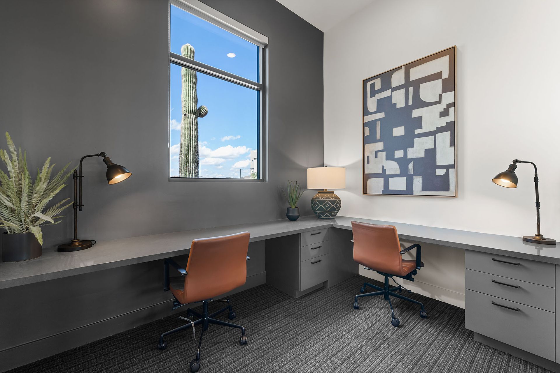 Office space with two desks, window view of cactus, gray walls, modern art, and black lamps at Marq Bronco Butte, offers brand-new apartments near TSMC in North Phoenix, AZ.