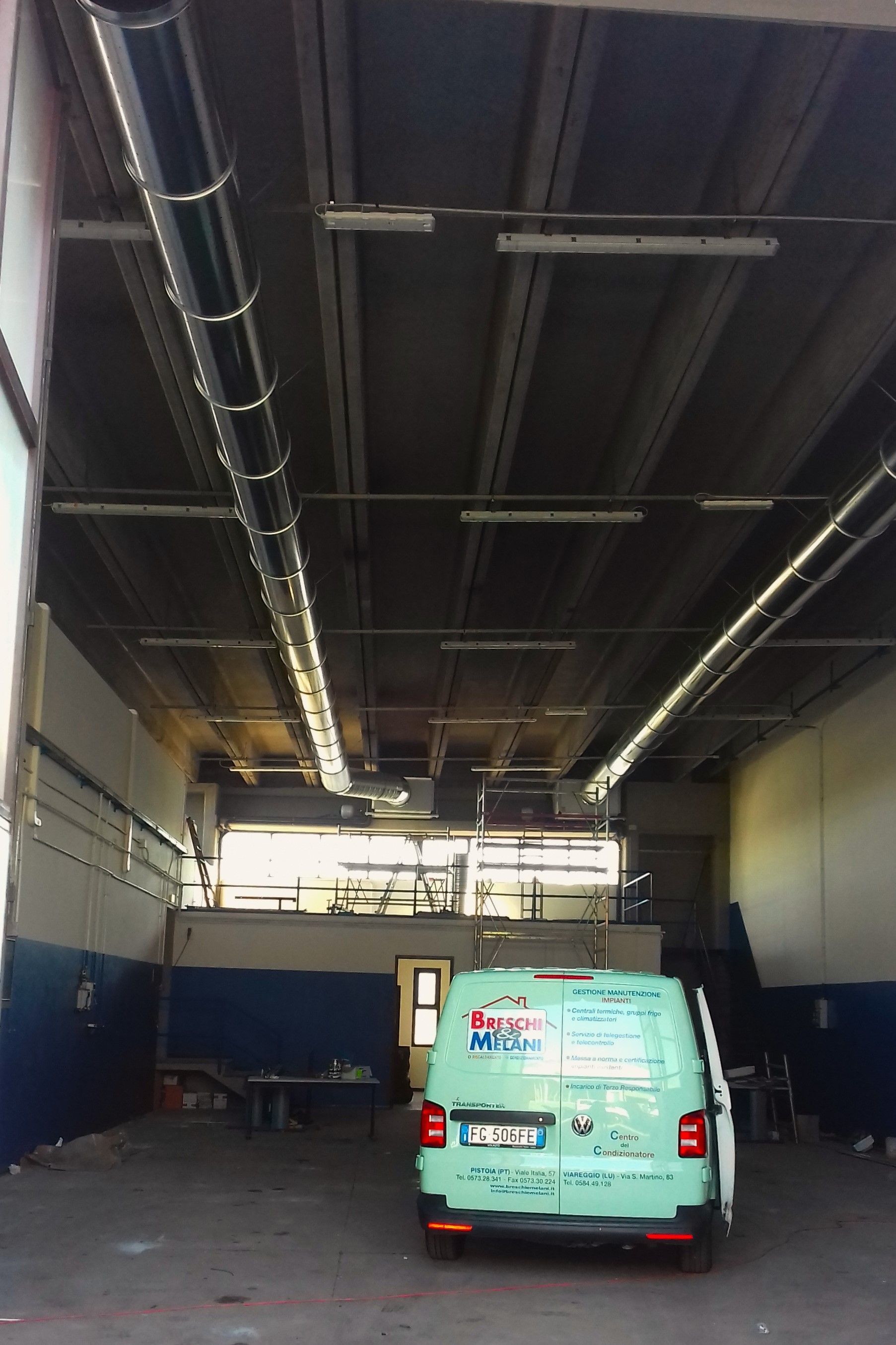 Furgone verde parcheggiato all'interno di un grande garage industriale con soffitto alto e tubature aeree.