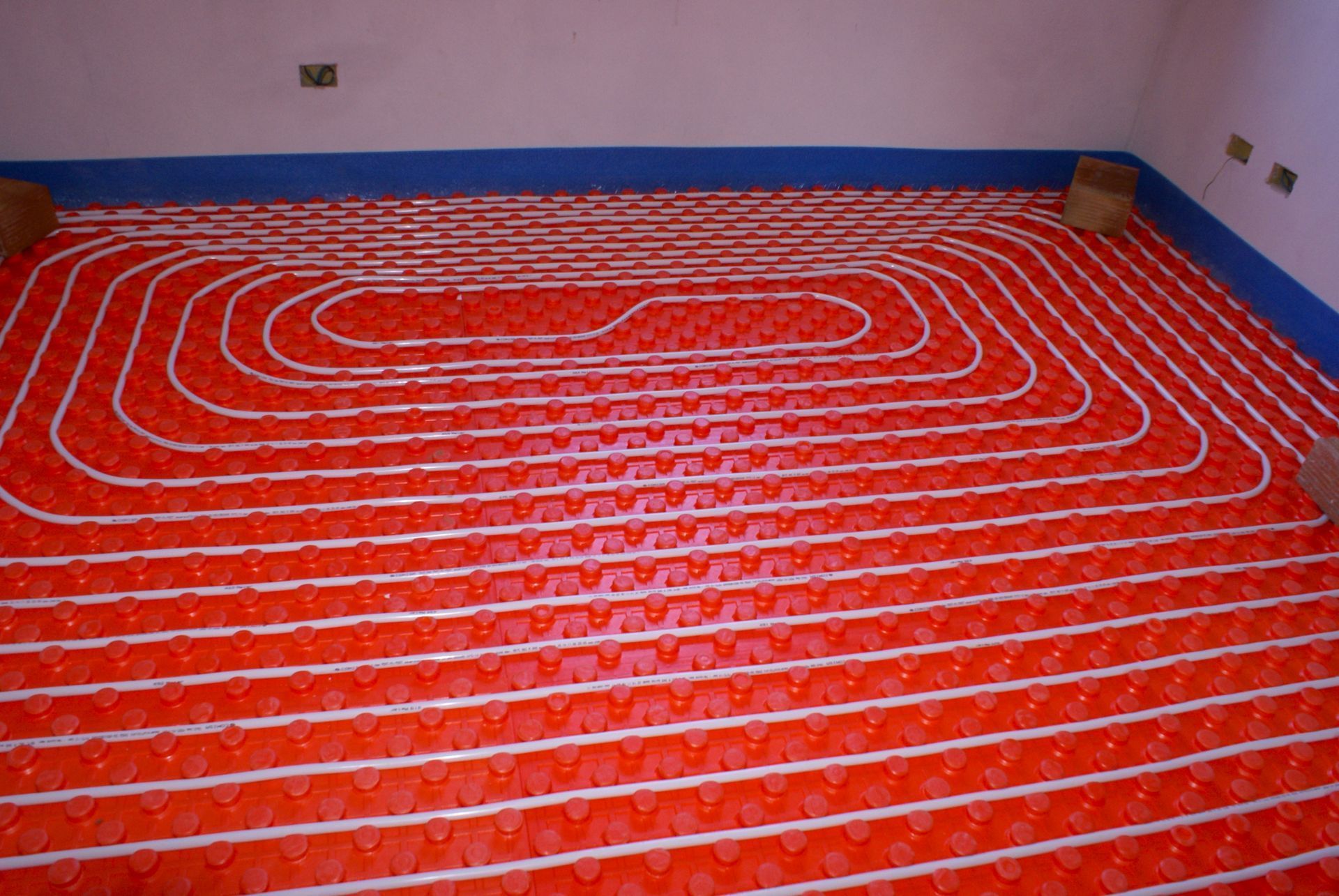 Tubi rossi per il riscaldamento a pavimento disposti a spirale sul pavimento di una stanza prima dell'installazione.