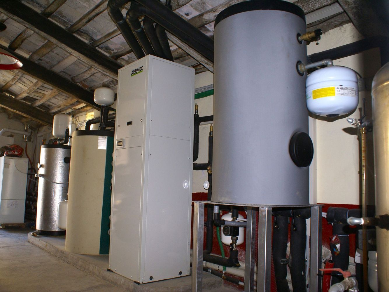 Locale caldaia industriale con grandi serbatoi e tubature sotto un soffitto inclinato.