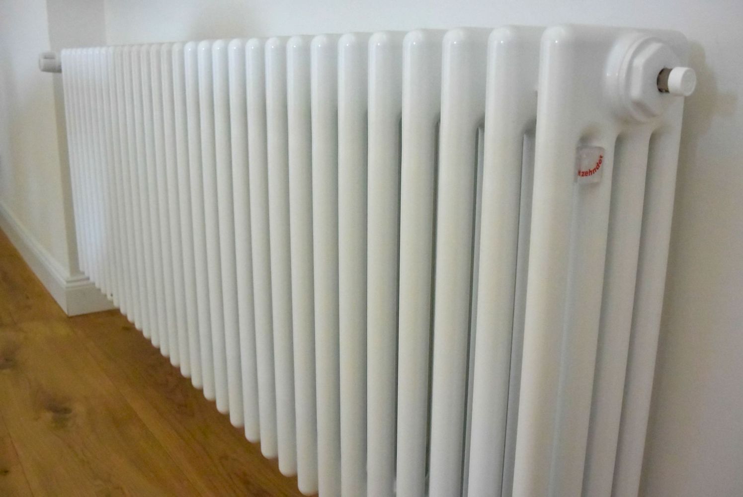 Radiatore bianco addossato a una parete in una stanza con pavimento in legno.