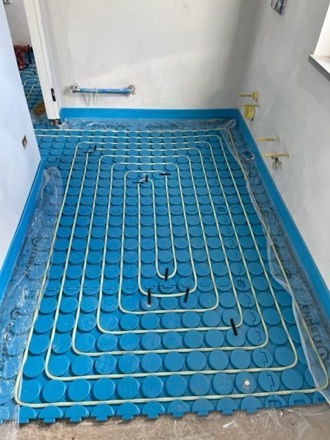 Tubi blu per il riscaldamento a pavimento posati in una stanza, disposti a spirale su pannelli isolanti.