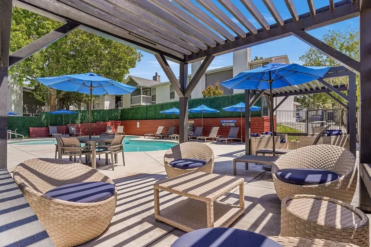 Outdoor seating area with lounge chairs and umbrellas next to a swimming pool.