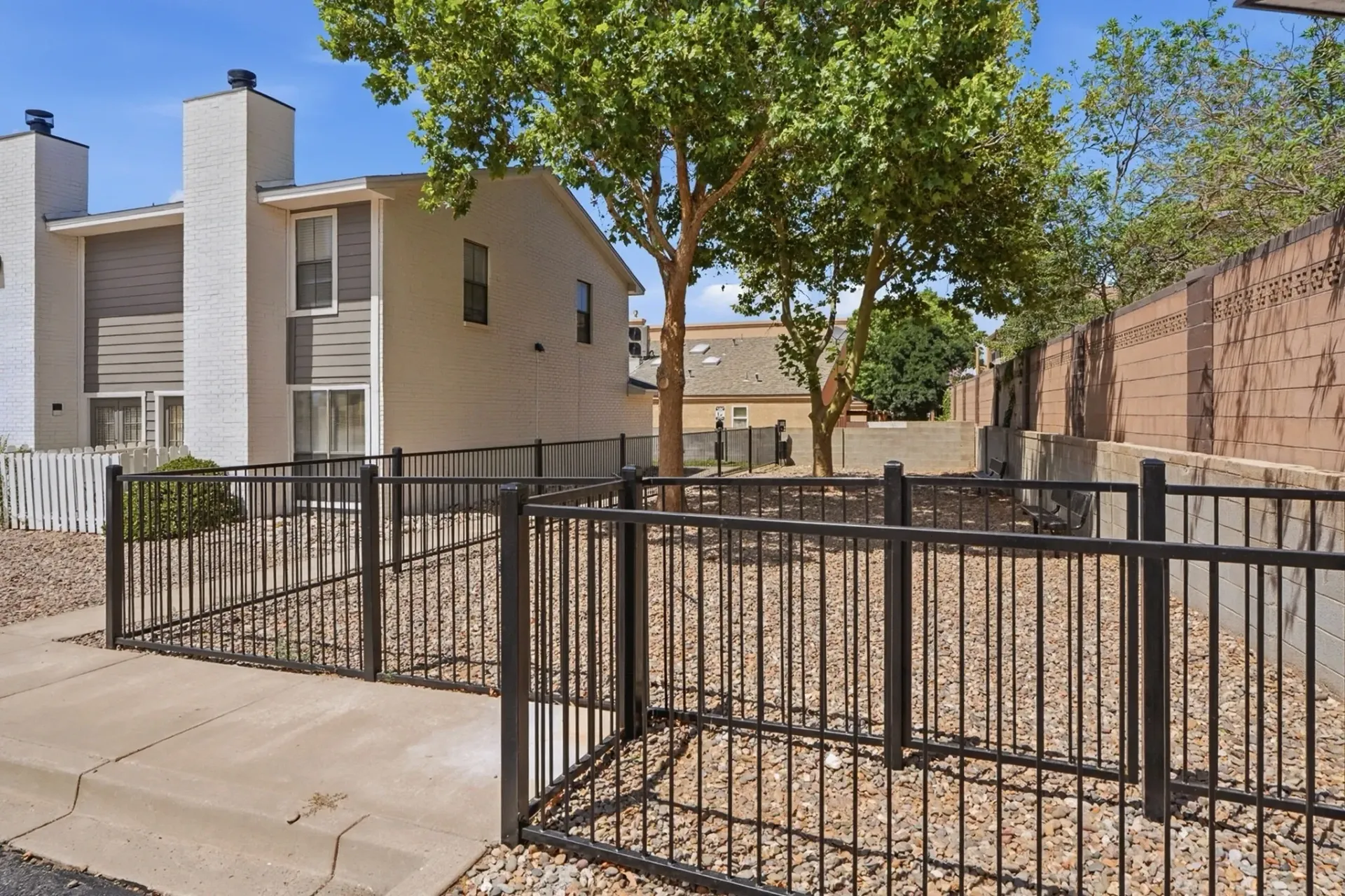 Fenced dog park area with trees and apartment buildings in the background.