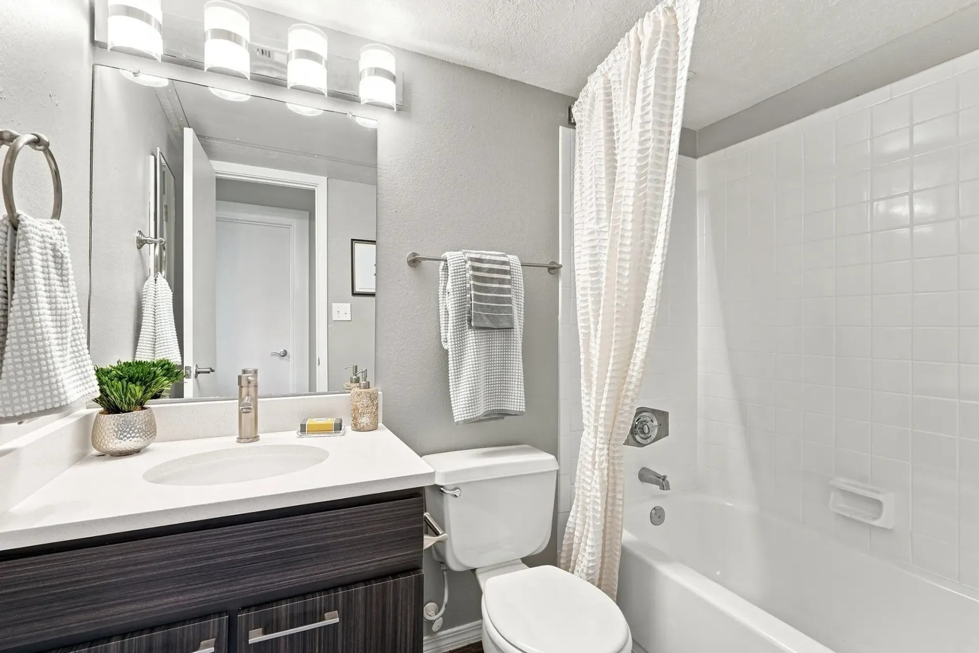 Modern bathroom with a single vanity, toilet, and bathtub with shower curtain.