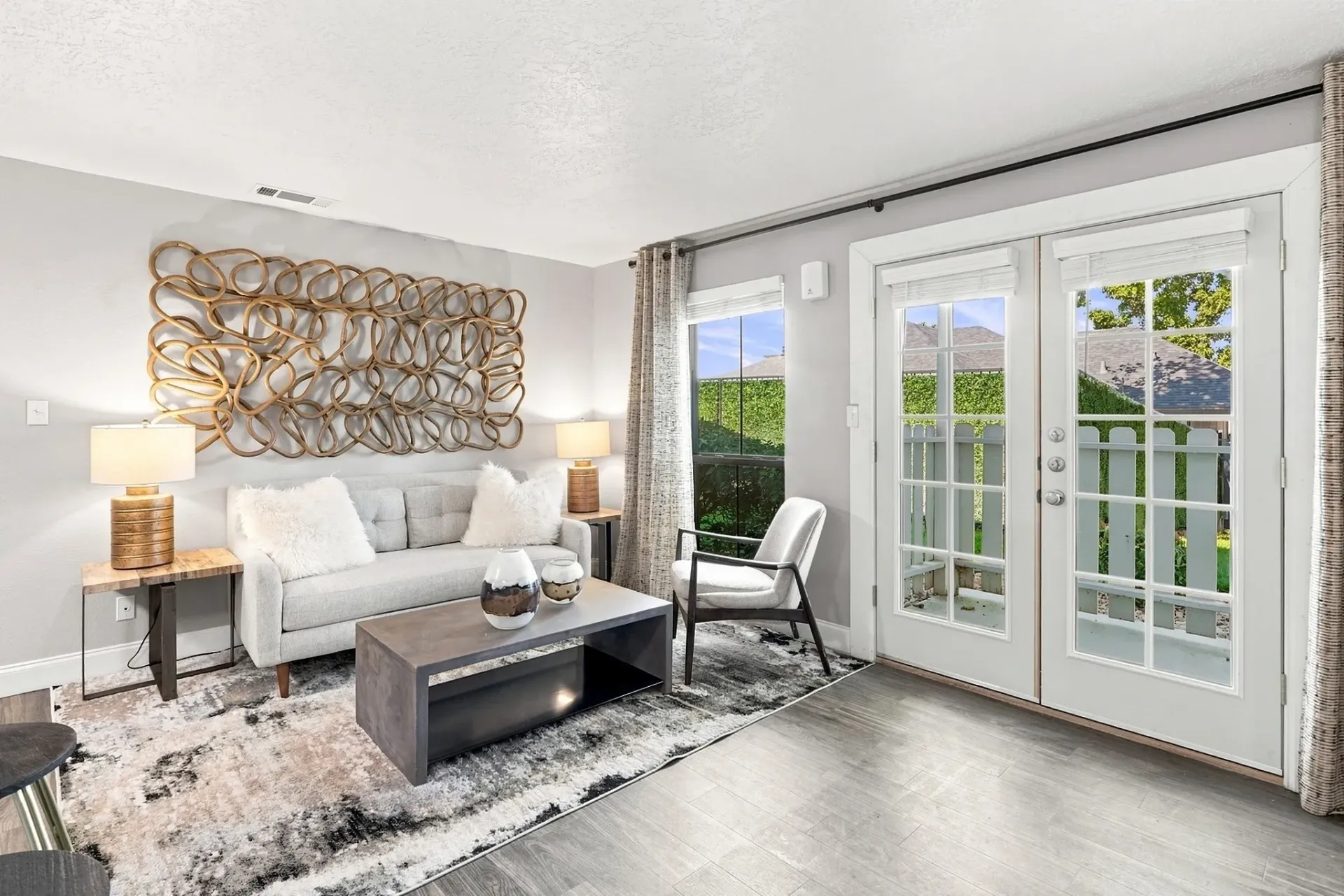 Living room with sofa, coffee table, and large window overlooking a backyard.