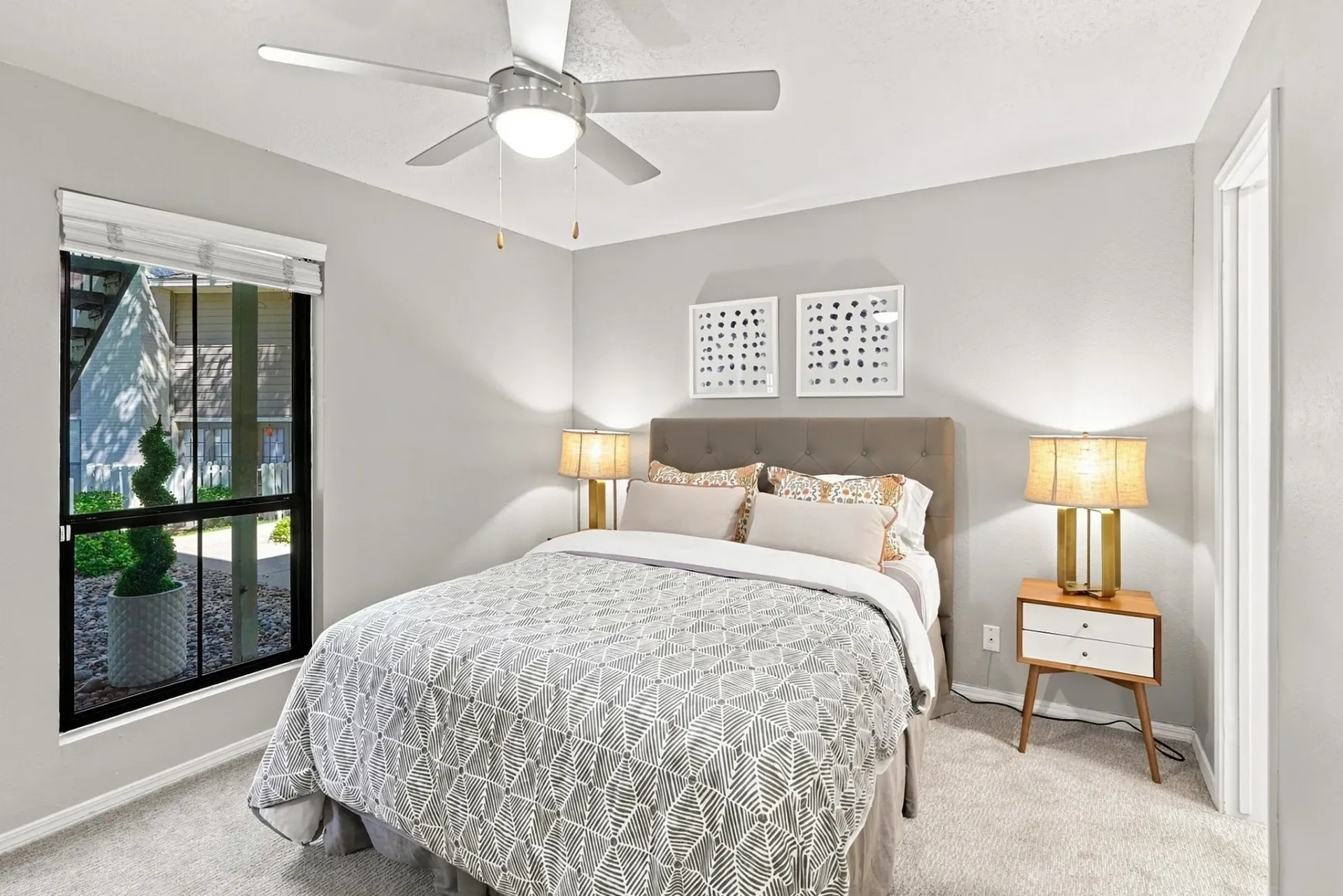A comfortable bedroom featuring a bed with patterned bedding, a ceiling fan, and a nightstand with a lamp.