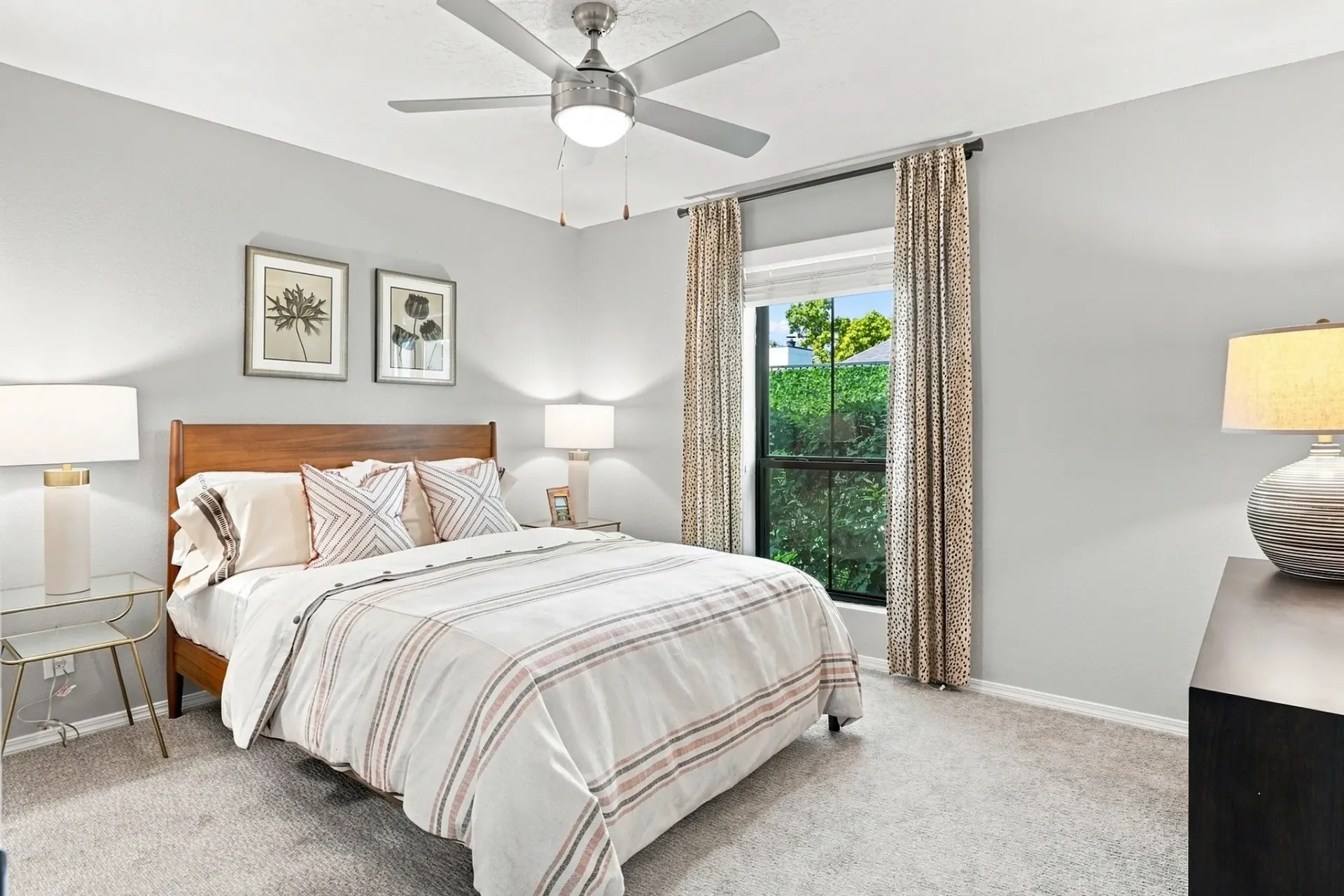 King-size bed with plush pillows and striped bedding in a well-lit bedroom with a ceiling fan and framed art.