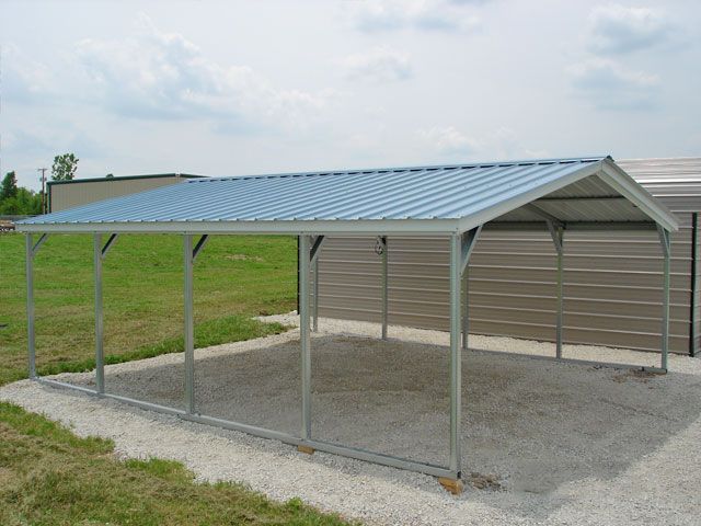 A carport is sitting in the gravel in front of a house