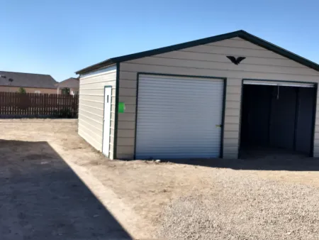 Small beige garage with two metal doors and a gravel driveway under a clear blue sky