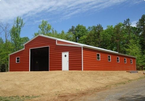 Red barn with white trim and open doors on a dirt lot under a blue sky