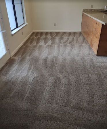 Woman vacuuming a white circular rug in a living room with brown furniture, kneeling.