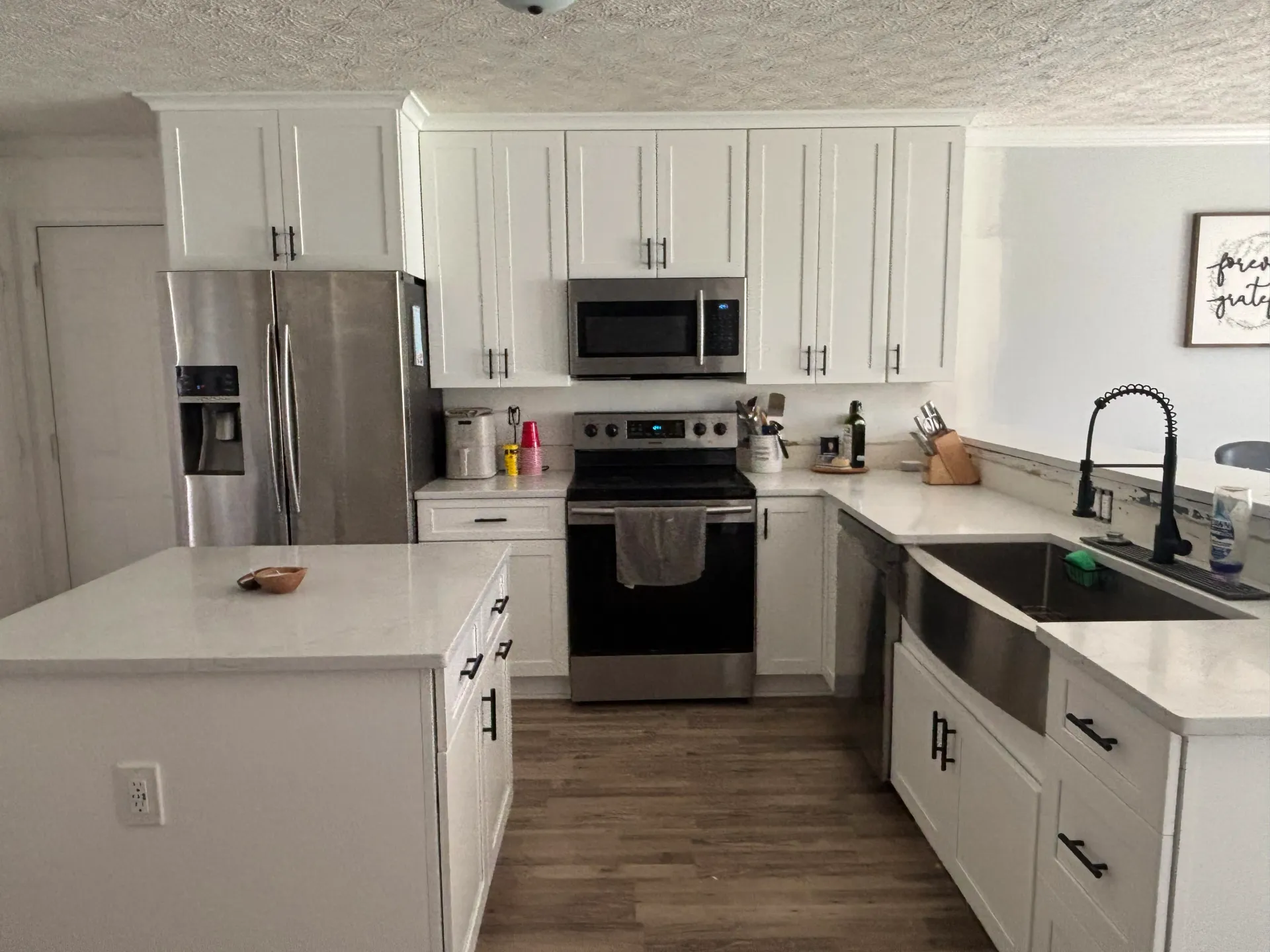 A modern kitchen featuring white cabinets, stainless steel appliances, a center island, and a farmhouse-style sink.