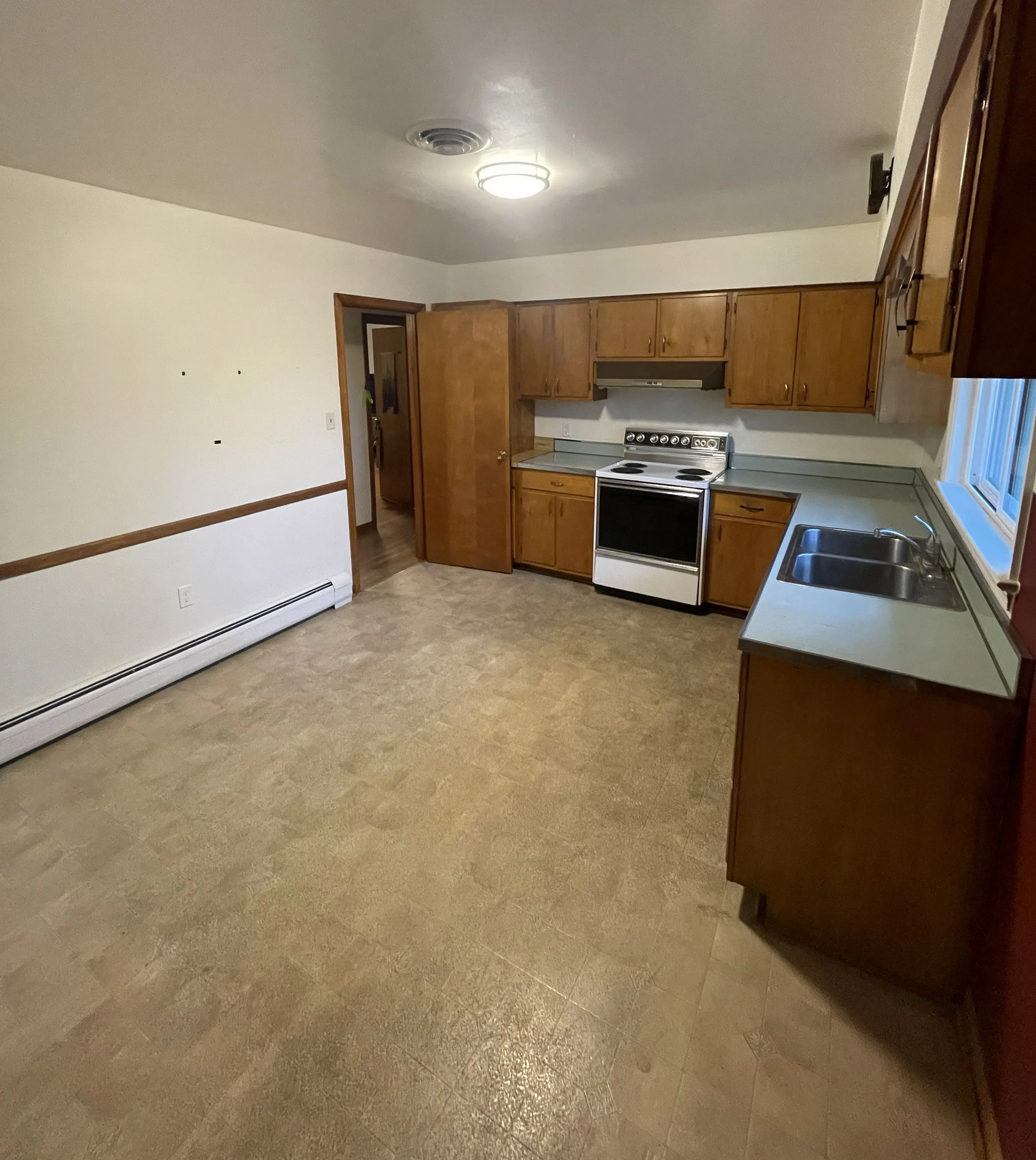 An open-concept kitchen with light wood cabinets, white walls, linoleum flooring, a gas stove, and a stainless steel sink.