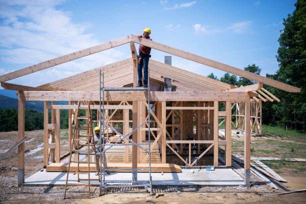 a man is standing on a ladder on top of a wooden house under construction