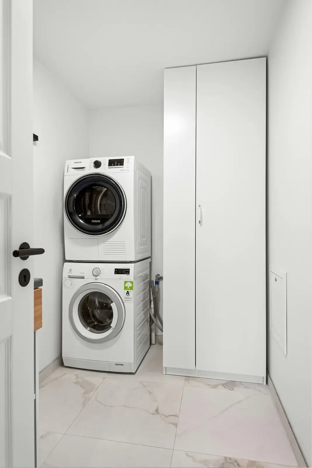 Stacked washer and dryer beside a tall white storage cabinet in a small laundry room