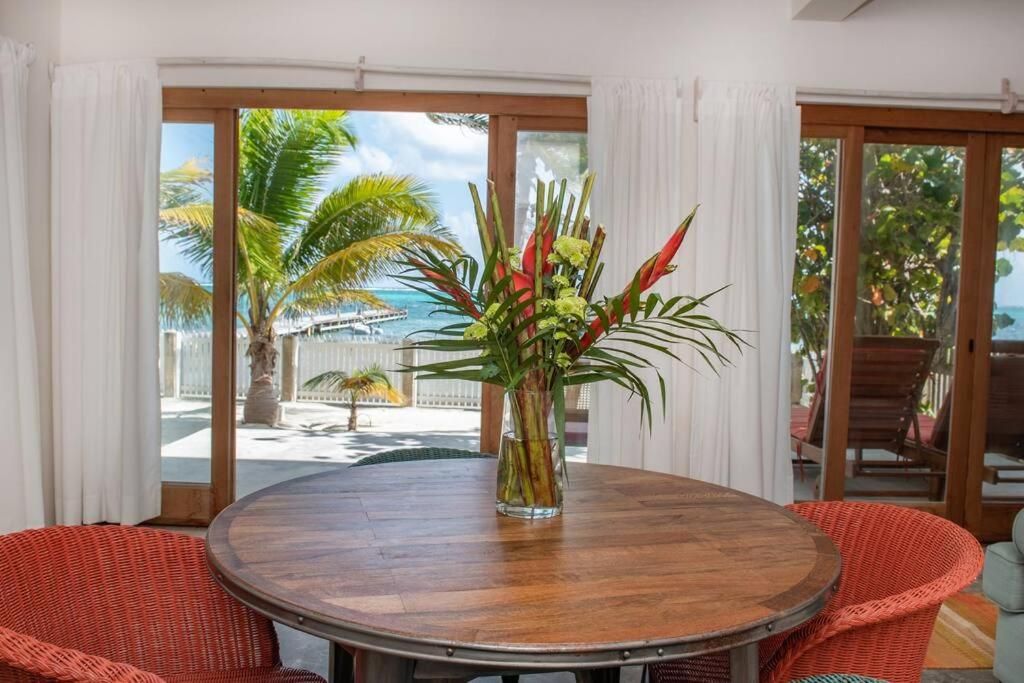 Round wooden table with flowers, two wicker chairs, and a view of a tropical beach through sliding glass doors.