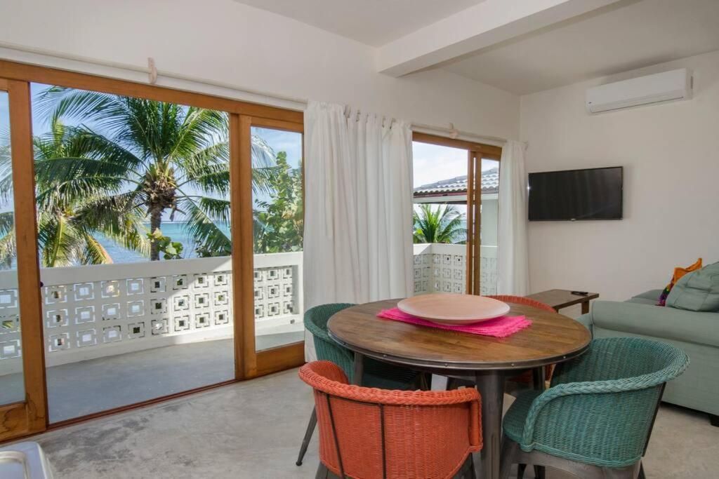 Bright dining area with ocean view from sliding doors, round table, colorful chairs.