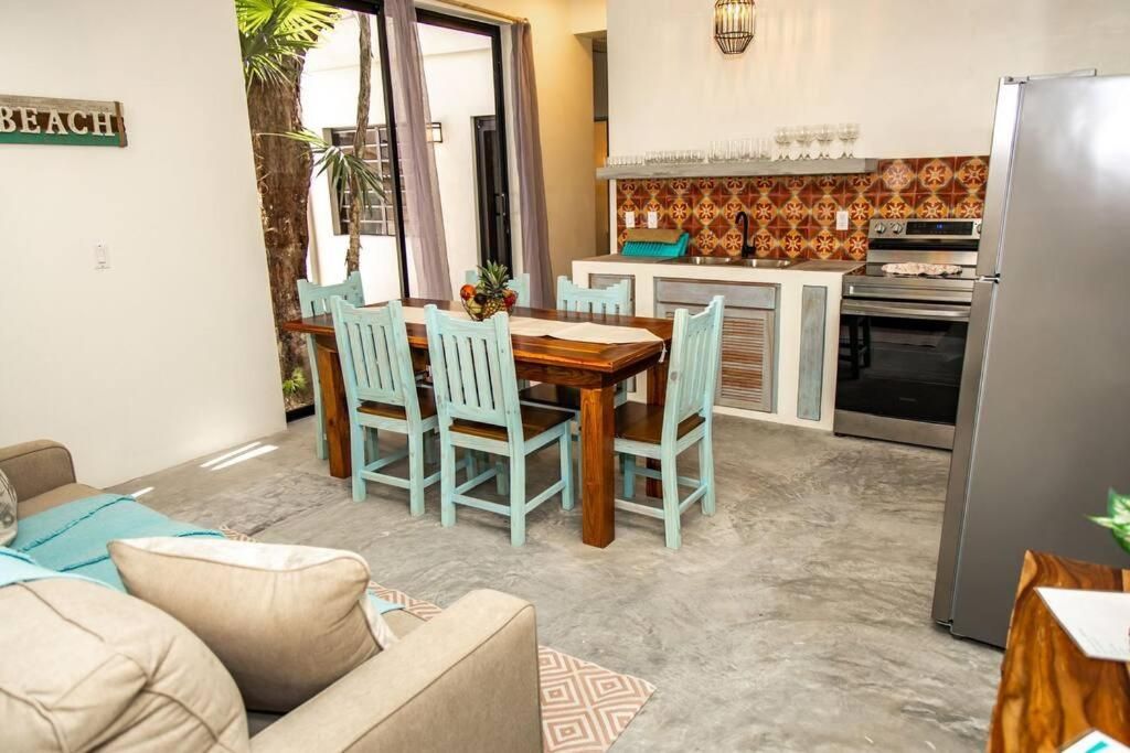 Open-plan kitchen and dining area with turquoise chairs, a wooden table, and a stainless steel refrigerator.