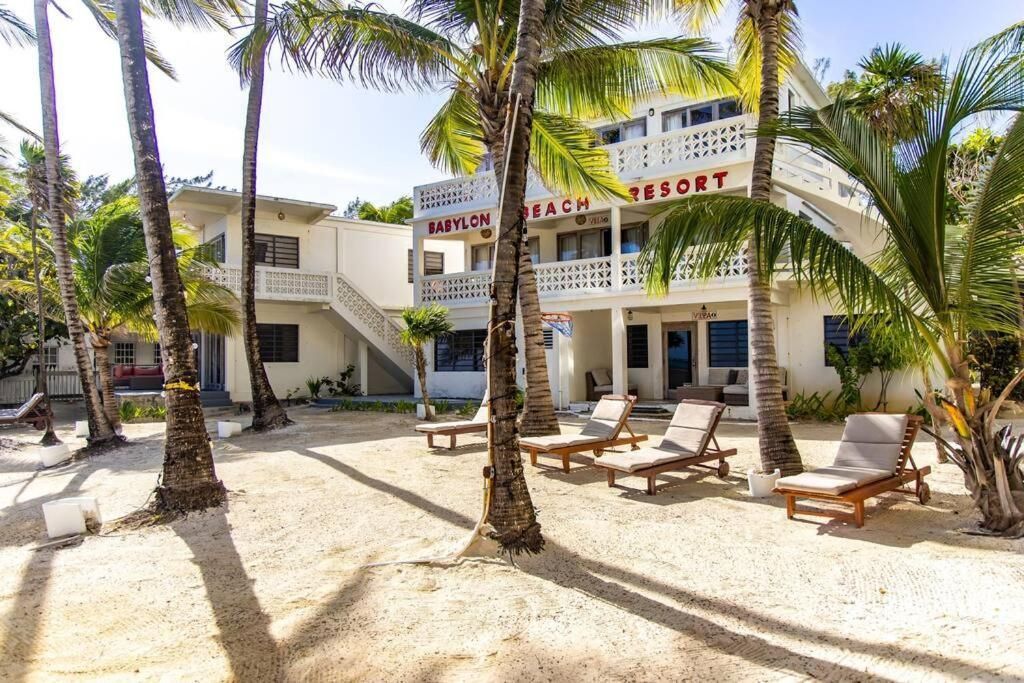 White beachfront resort with palm trees and lounge chairs.