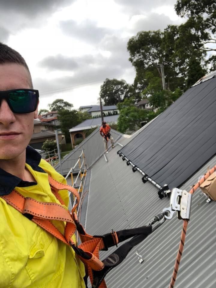 A Man Wearing Sunglasses Is Standing On Top Of A Roof — CJ Electrical & Solar In Belmont, NSW