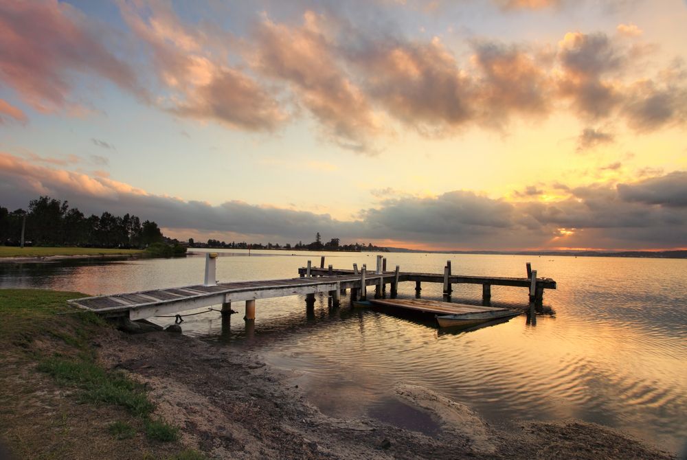 A Wooden Dock In The Middle Of A Lake At Sunset — CJ Electrical & Solar In Belmont, NSW