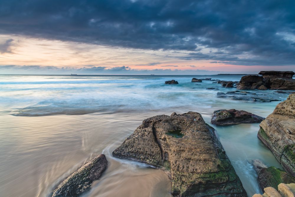 A Long Exposure Photo Of A Rocky Beach At Sunset — CJ Electrical & Solar In San Remo, NSW