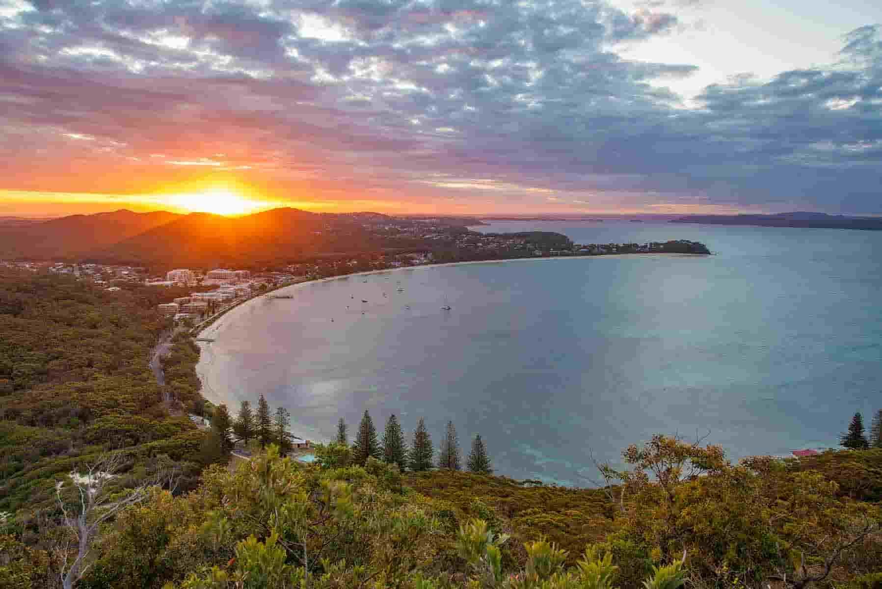 The Sun Is Setting Over A Large Body Of Water Surrounded By Trees — CJ Electrical & Solar In Nelson Bay, NSW