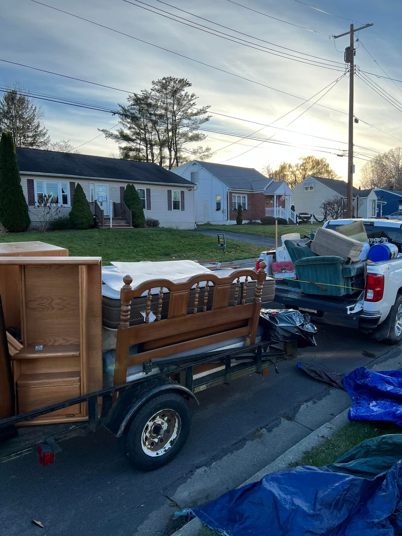 A truck bed overflowing with trash, including a trampoline and bags, parked on a road.