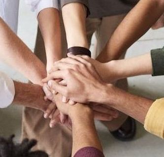Photograph of multiple hands stacked one on top of the other, signifying unity.
