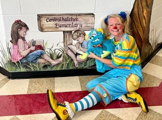 A clown is sitting on the floor holding a stuffed animal.