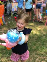 A little girl is holding a balloon in the shape of a pig.