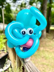 A blue balloon with big eyes is sitting on a wooden railing.