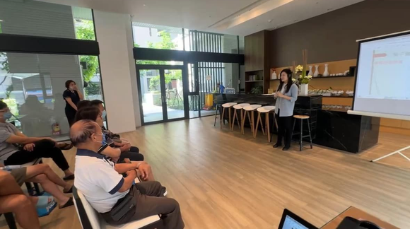 詠華地政士事務所所長－鄭秀慧女士在現代化的會議空間裡，透過投影螢幕向就座的觀眾講解地政相關知識。