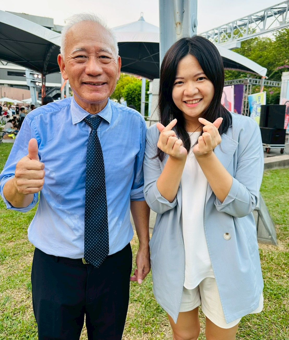戶外，一名身穿藍色襯衫的男子豎起大拇指大力推薦，詠華地政士事務所所長－鄭秀慧女士在旁用手指比劃出愛心。