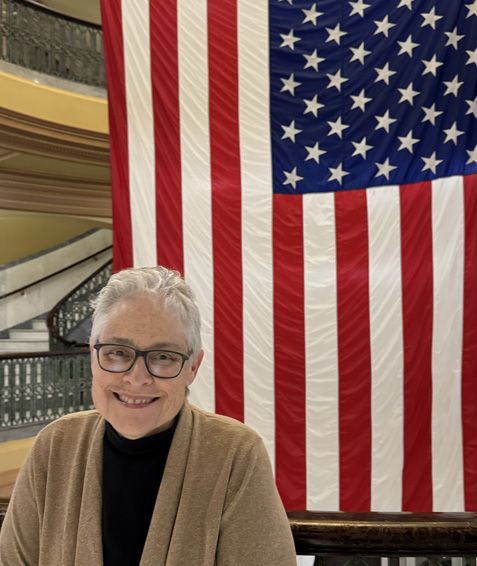 Smiling person in glasses before a large American flag in an indoor stairwell