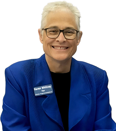 Karen Whitney, wearing a blue blazer and glasses, smiles at the viewer. A name tag reads 