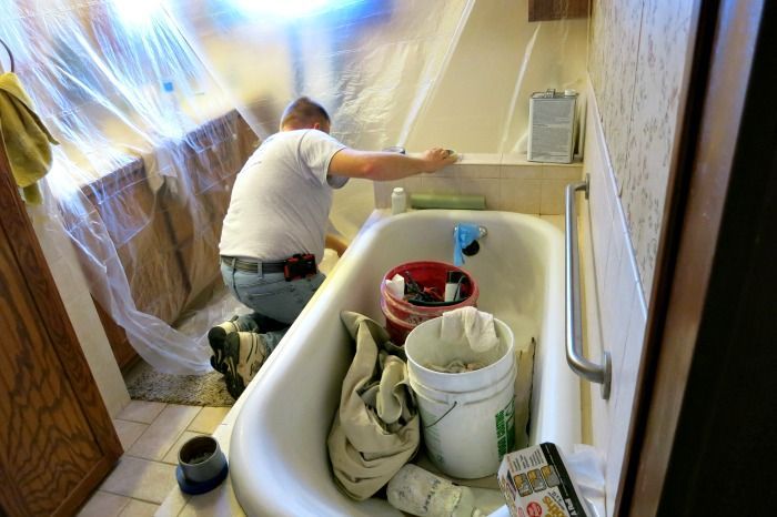 A man is kneeling over a bathtub in a bathroom.