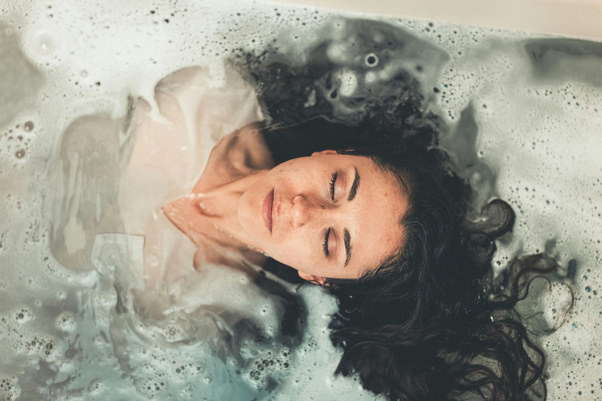 A woman is laying in a bathtub with her eyes closed.