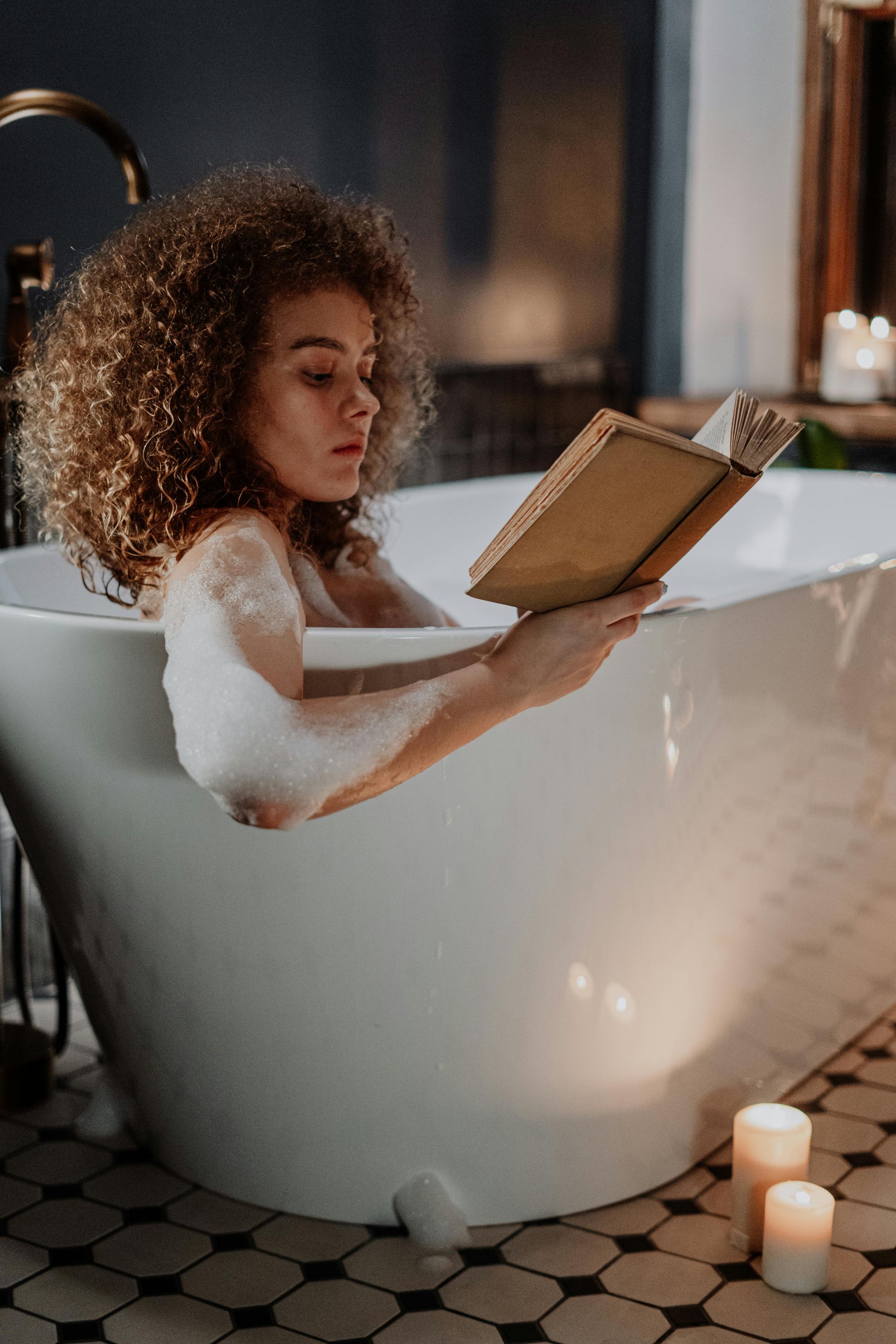 A woman is sitting in a bathtub reading a book.
