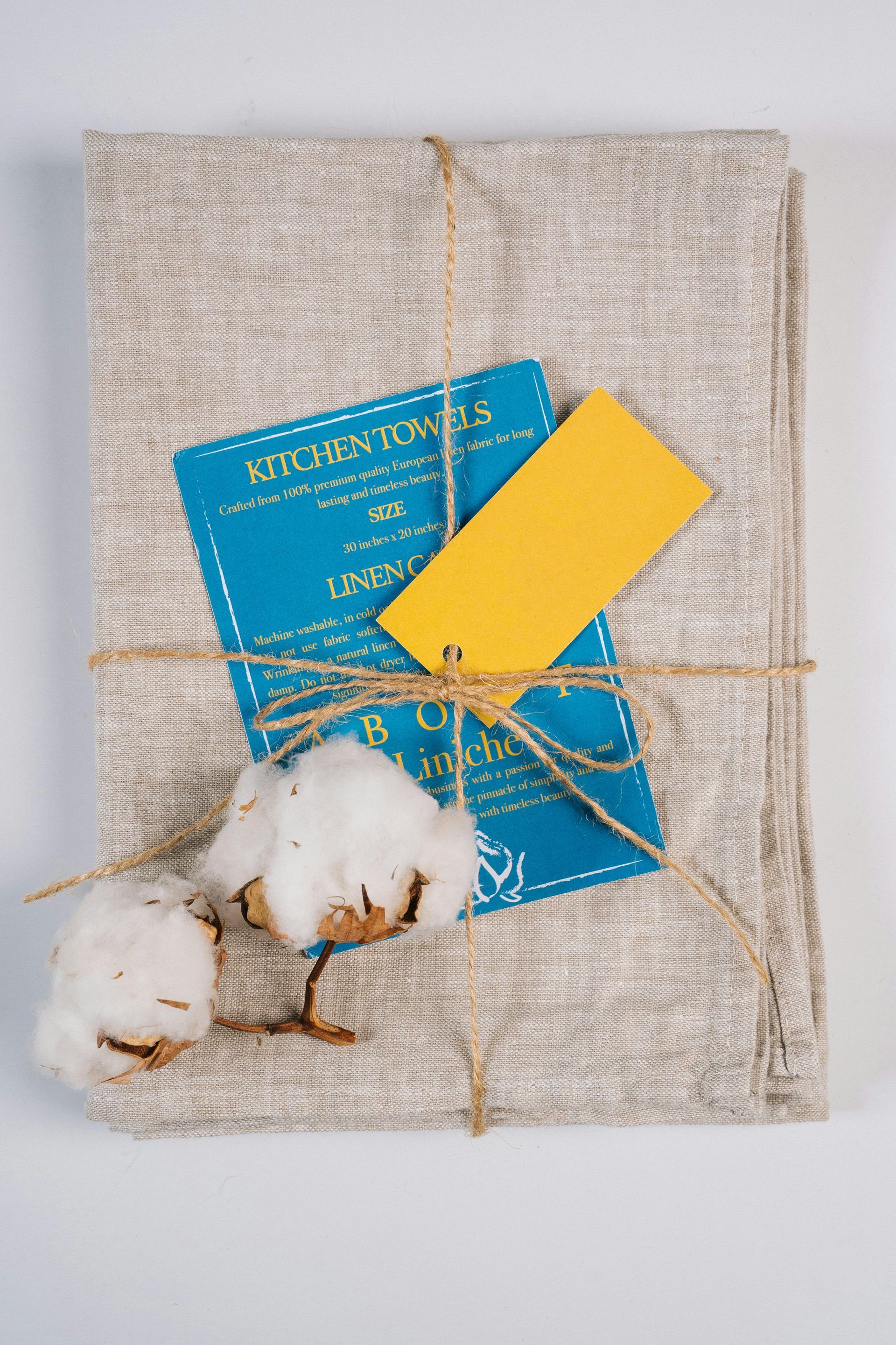 A towel with a yellow tag tied to it and cotton flowers.