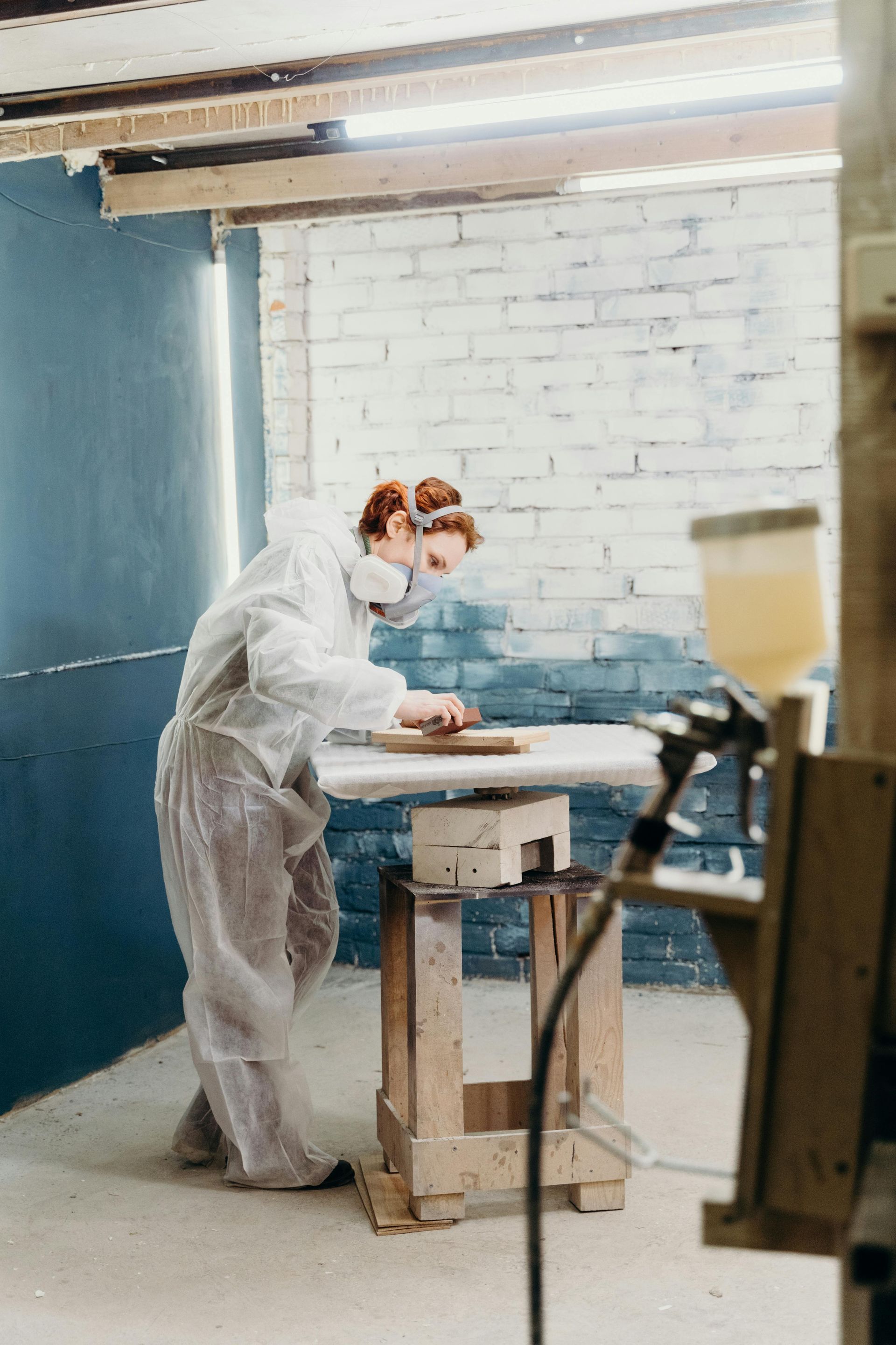 A man in a protective suit is working on a wooden table in a workshop.