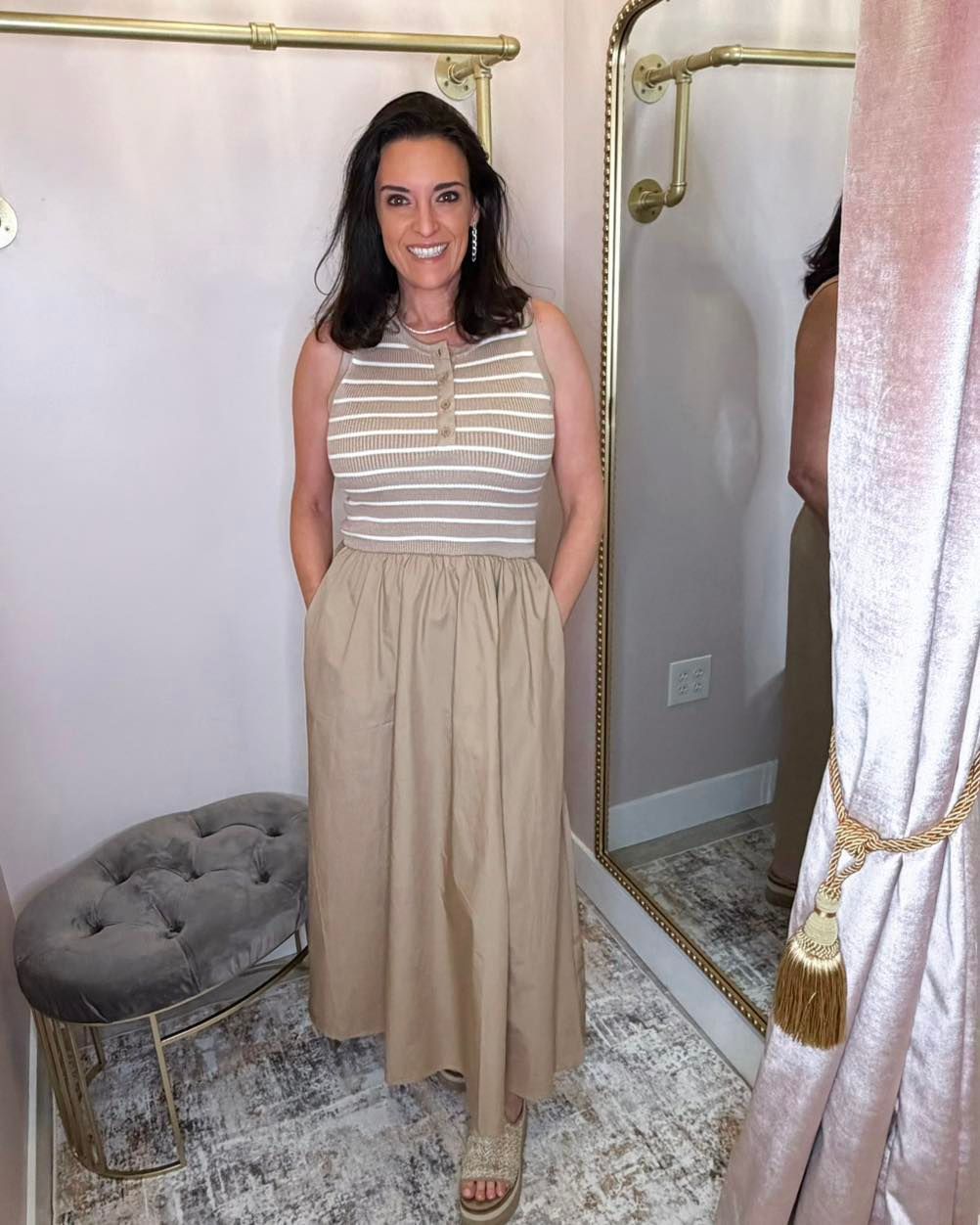 Woman standing in a fitting room wearing a striped sleeveless top and beige skirt