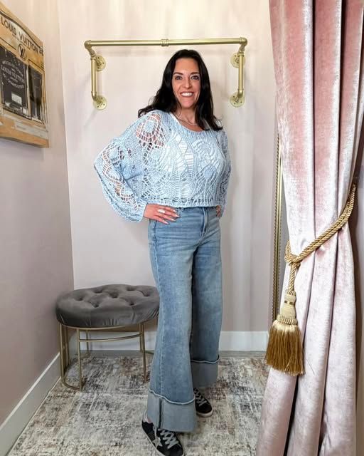 Woman posing in a light blue lace blouse and flared jeans in a pink-curtained room