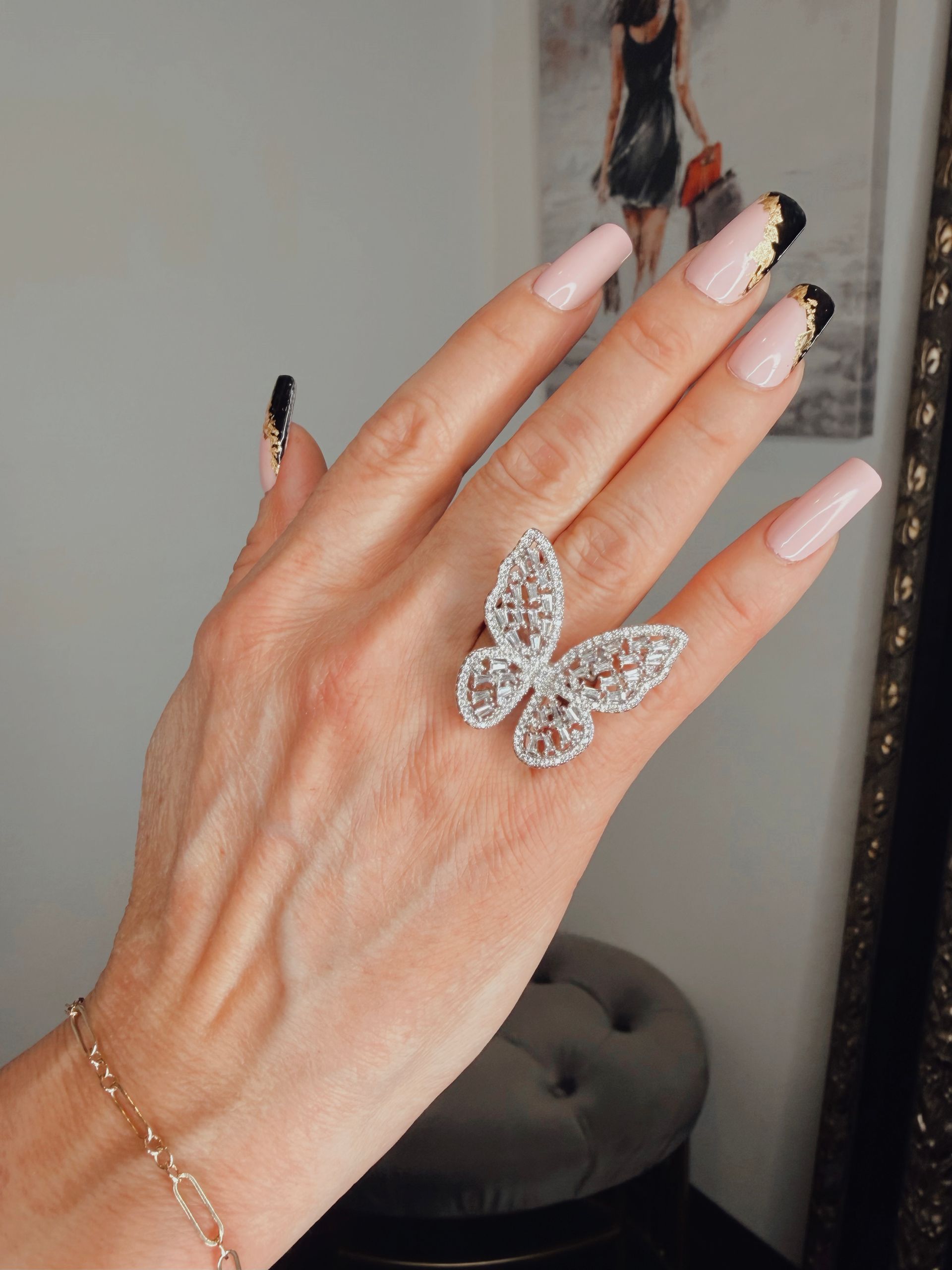 Hand with long manicured nails wearing a butterfly ring and gold bracelet