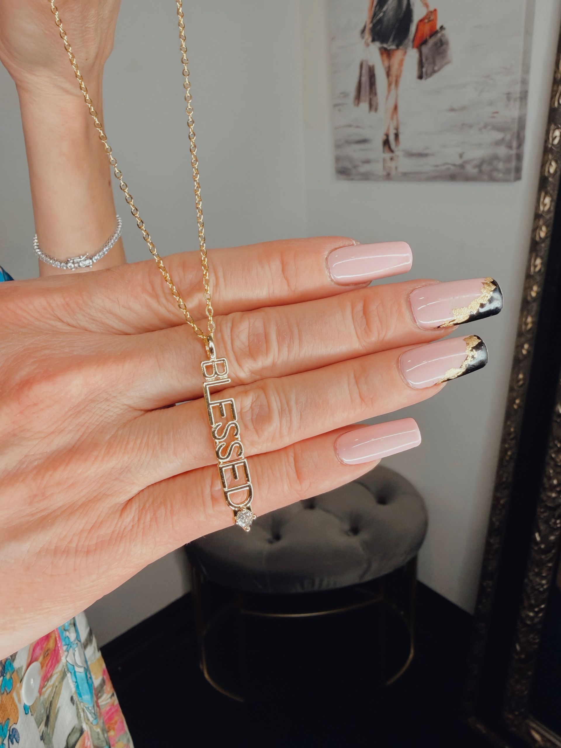 Hand holding a gold chain necklace over long pink nails with black tips in a mirrored room