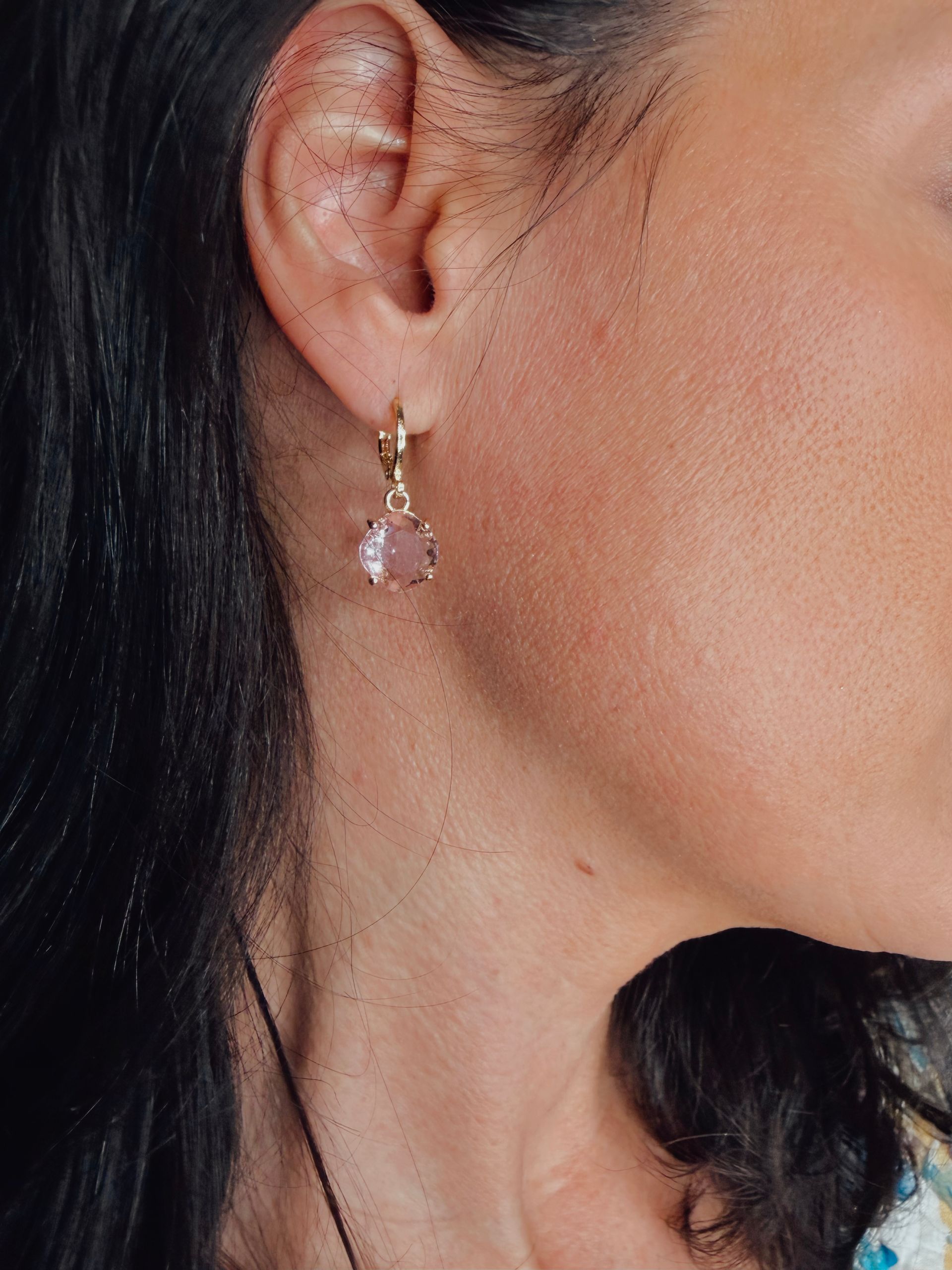 Close-up of a woman’s ear wearing a small pink drop earring and gold hoop earring